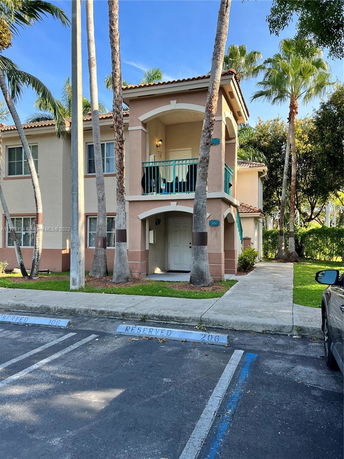 Front view of a two-story house with a balcony and palm trees.