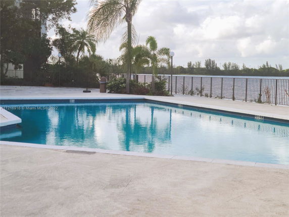 Outdoor swimming pool area with surrounding fence and palm trees.