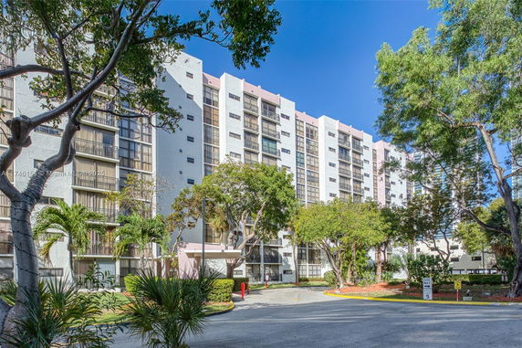 Front view of a multi-story residential building with large windows and surrounded by trees.