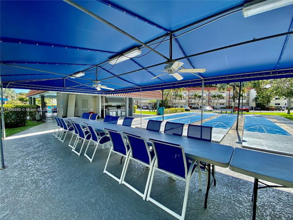 Outdoor covered seating area with table and chairs, located next to shuffleboard courts.