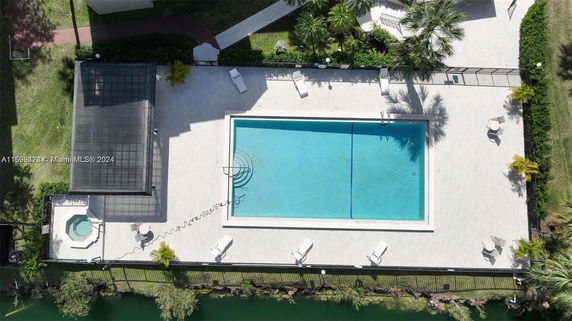 Aerial view of a swimming pool area with surrounding sun loungers and nearby greenery.
