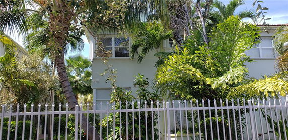 Front view of a two-story house partially obscured by dense greenery and a fence.