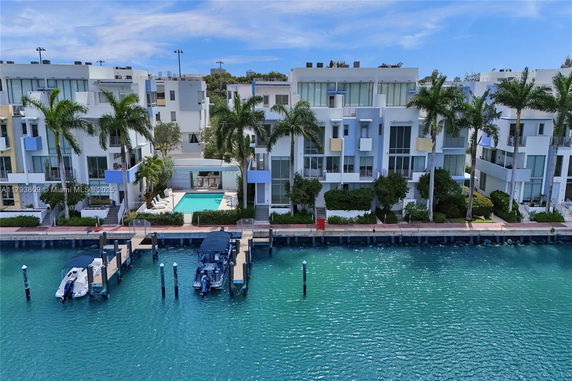 Front view of multiple-story waterfront buildings with balconies and palm trees.