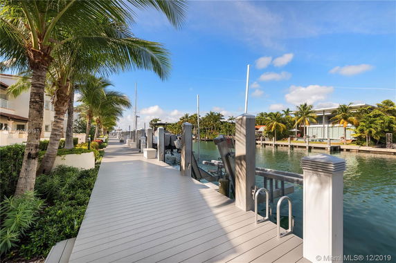 Waterfront walkway with palm trees and adjacent residential buildings.