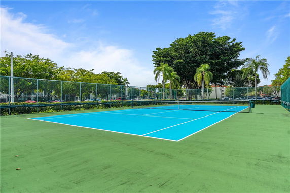 Tennis court with blue surface surrounded by trees and fencing.