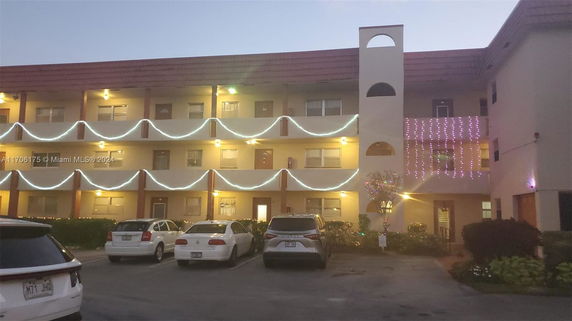 Front view of a multi-story building with decorative lights and a parking area.