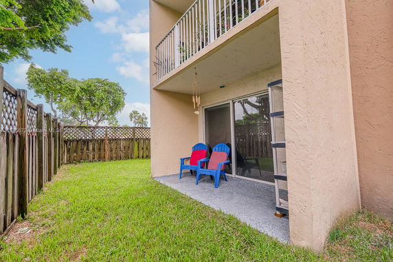 Exterior view showing a ground floor patio area with sliding doors, two chairs, and a wooden fence encircling a small lawn.