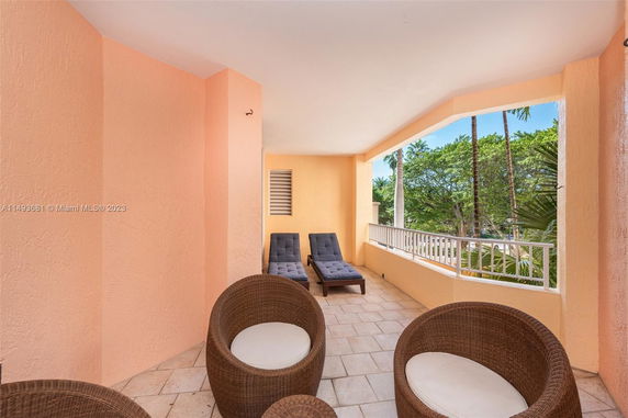 Outdoor balcony area with wicker chairs and lounge chairs, surrounded by coral-colored walls and a view of palm trees.