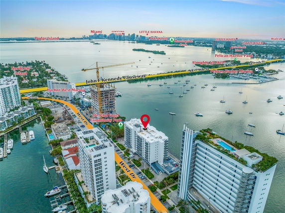 Panoramic view of high-rise buildings overlooking a water body with numerous boats and a distant city skyline.