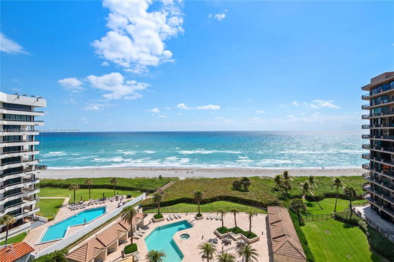 Panoramic view of ocean from a high building with pools and green areas below.