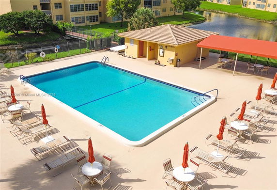 Outdoor swimming pool area with lounge chairs and umbrellas, adjacent to a building.