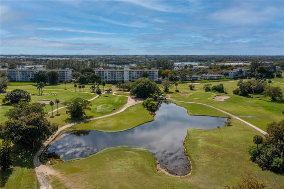 Aerial view of apartment buildings surrounded by a golf course with a small lake.