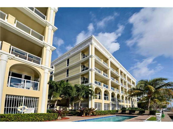 Front view of a multi-story building with balconies and arches, surrounded by palm trees.