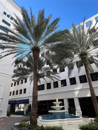 View of a multi-story building with palm trees and a fountain in the foreground.