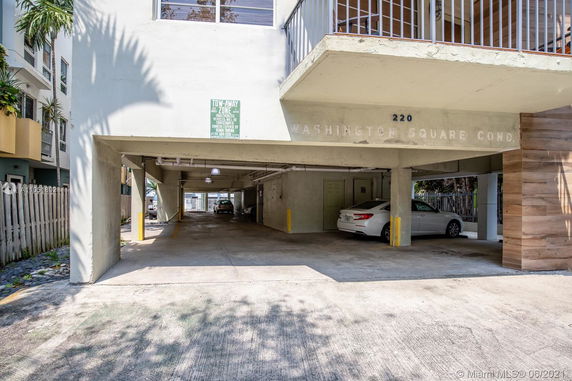 Outdoor parking area beneath a building with vehicles parked.