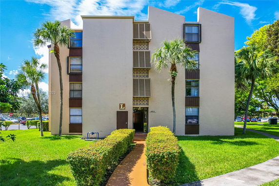 Front view of a mid-rise apartment building with minimalistic design and palm trees in front.