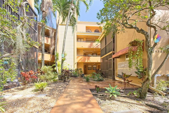 Front view of a multi-story residential building with balconies and surrounding greenery.