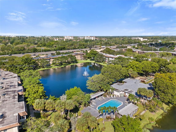 Aerial view showing a residential area with a pond and swimming pool surrounded by buildings and trees.