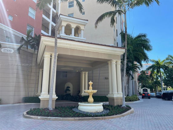 Front view of a multi-story building entrance with columns and a decorative fountain.