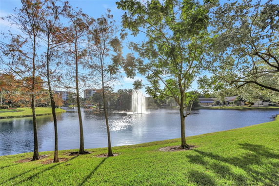 View of a pond with a fountain and trees nearby.