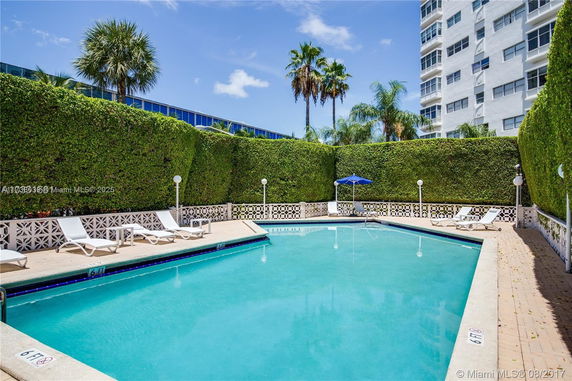 Outdoor swimming pool area with lounge chairs and hedge privacy walls.