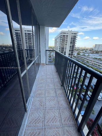 View from a building balcony showing a tiled floor and railing with nearby buildings and parking area visible.