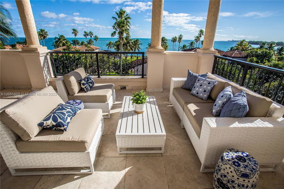 Balcony with outdoor seating overlooking the ocean and palm trees.