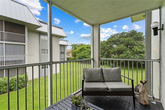 View from a balcony with seating area overlooking grassy area and adjacent buildings.