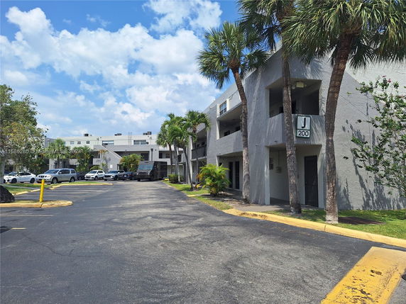 Front view of a two-story residential building with a parking area and palm trees.