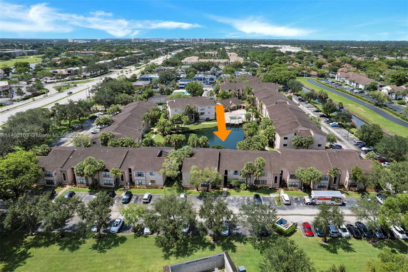 Aerial view of a residential community with multiple buildings, a parking area, and a central pond.