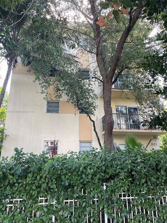 Front view of a multi-story residential building partially obscured by trees and a fence.