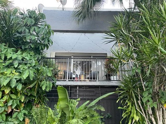 Front view of a two-story building with a balcony surrounded by greenery.