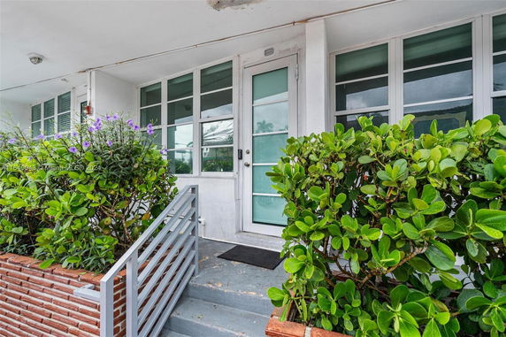 Front view of a house entrance with glass door and surrounding plants.