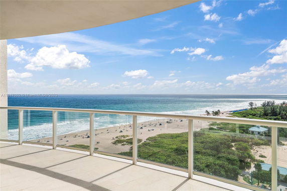 Panoramic view of a beach and ocean from a balcony with glass railing.
