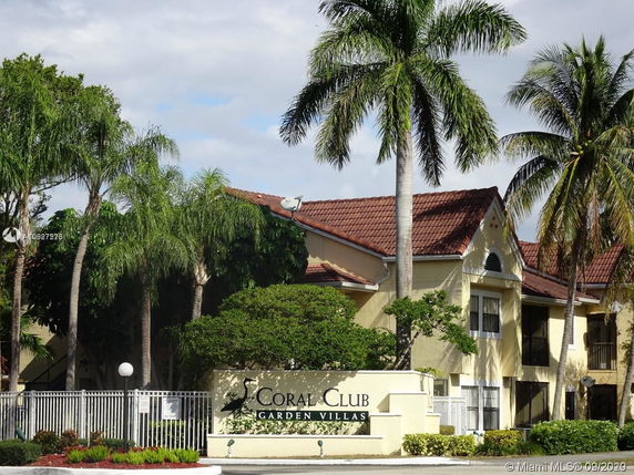 Front view of a multi-story villa with a red-tiled roof and surrounding palm trees.