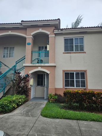 Front view of a two-story house with an external staircase and arched entryway.
