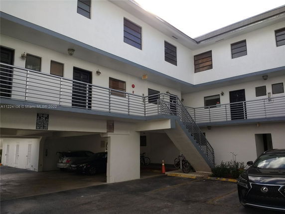 Outdoor parking area with parked cars and a two-story building with stairs and a railing.