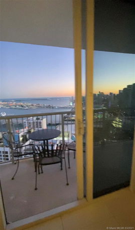 Panoramic view from a balcony showing a cityscape and waterfront at sunset.
