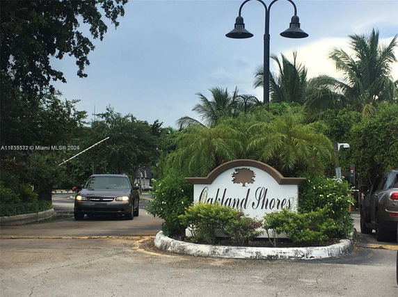 Entrance sign for a residential community named Oakland Shores, surrounded by palm trees and greenery.