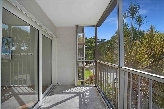 Balcony with metal railing and glass doors overlooking trees and neighboring buildings.