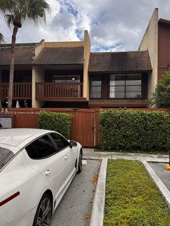 Front view of a two-story building with wooden balcony and parking area.