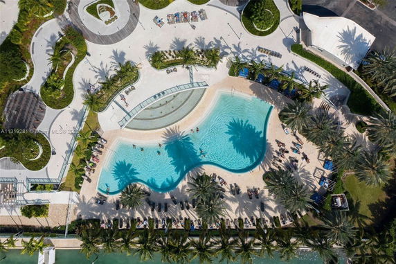 Aerial view of a large rooftop swimming pool surrounded by palm trees and sun loungers.
