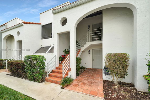 Front view of a two-story white building with an arched entrance and tiled steps.