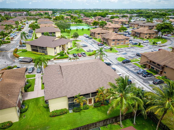 Aerial view of a residential complex with multiple buildings, parking areas, and surrounding greenery.