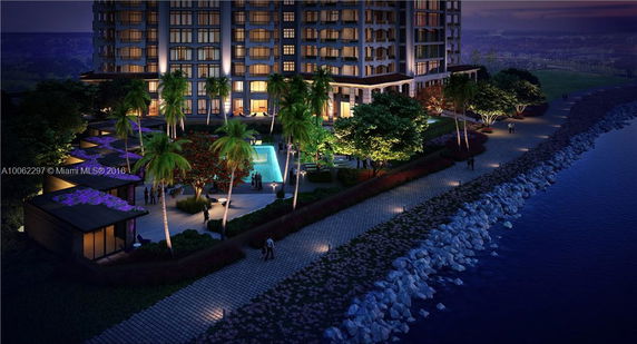 Exterior view of a high-rise building with a lit courtyard and a pathway by the waterfront.