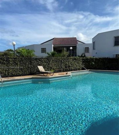 Outdoor swimming pool with clear water and a lounge chair by the poolside, surrounded by a hedge.