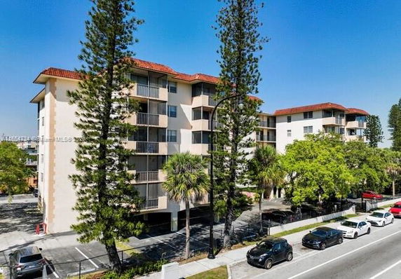 Front view of a multi-story apartment building with balconies and a red-tiled roof.