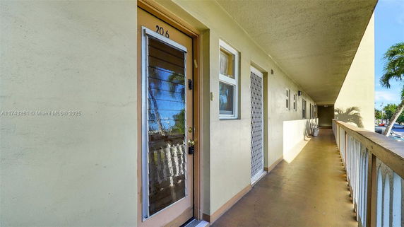 Exterior view of an apartment hallway on an upper level, showing doors and windows along the walkway.