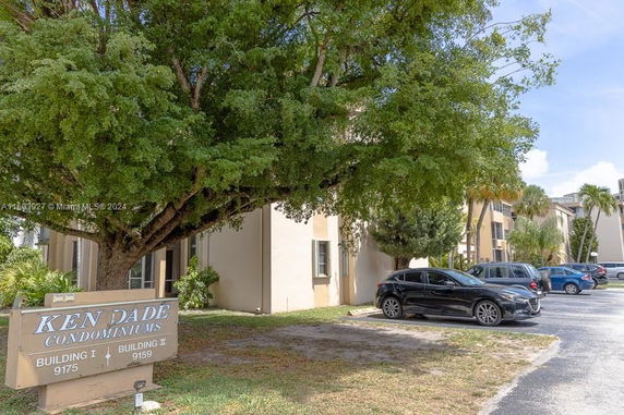Exterior view of condominium buildings with a parking area and trees.