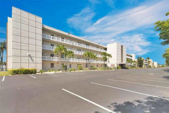 Front view of a multi-story building with balconies and a parking area.